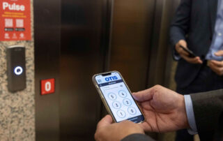 usuario frente a un ascensor con aplicación Pulse instalada en su teléfono móvil